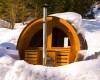 Drewniana sauna w kształcie beczki otoczona śniegiem w lesnym otoczeniu.