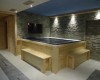 Jacuzzi otoczone drewnianymi ławkami w pomieszczeniu z kamiennymi ścianami.