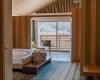 Nowoczesny pokój hotelowy z drewnianymi meblami, widokiem na góry i balkonem z fotelem.