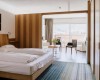 Pokój hotelowy z łóżkiem małżeńskim, stołem i krzesłami, balkonem oraz widokiem na góry.