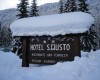 Drewniana tablica hotelu S. Giusto pokryta śniegiem w zimowym krajobrazie.
