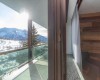 Widok z okna na ośnieżone góry i balkon ze szklanym balustradą.