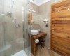 Mała łazienka z przeszklonym prysznicem i drewnianymi elementami.