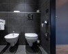 Nowoczesna łazienka z bidetem i toaletą na czarnych kafelkach.