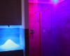Nowoczesna kabina prysznicowa z kolorowym oświetleniem w odcieniach niebieskiego i fioletowego.  