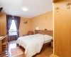 Pokój z podwójnym łóżkiem, biurkiem i balkonem, na ścianie wisi krzyż.