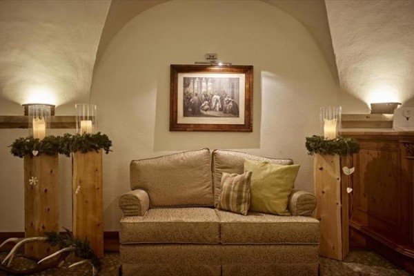 Sofa z poduszkami pomiędzy dwoma drewnianymi filarami z dekoracjami, nad sofą wisi obraz.