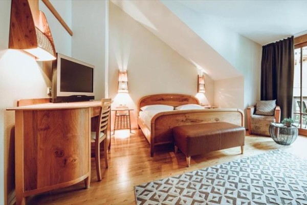 Nowoczesny pokój hotelowy z drewnianymi meblami, łóżkiem, telewizorem i drzwiami balkonowymi.