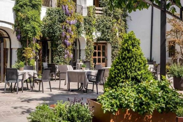 Zewnętrzny taras restauracji otoczony zielenią z jadalnymi stołami.