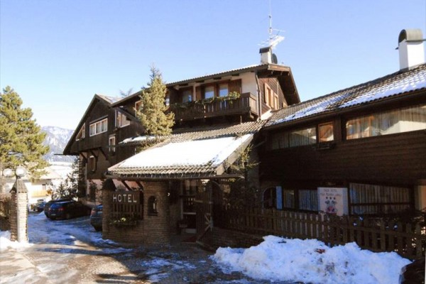 Drewniany górski hotel z miejscami parkingowymi, otoczony śniegiem i drzewami.