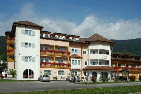 Hotel z balkonami i kwiatami z przodu, otoczony górami.