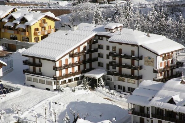 Ośnieżony hotel górski otoczony innymi budynkami w zaśnieżonym krajobrazie.
