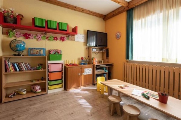 Pokój dziecięcy z meblami, zabawkami i oknem z półprzezroczystymi zasłonami.
