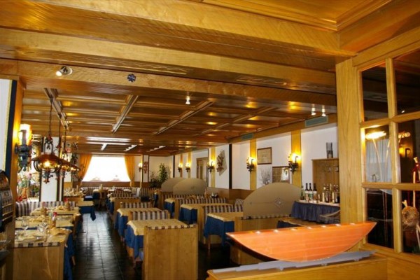 Wnętrze restauracji z drewnianymi stołami i sufitem, niebieskimi obrusami oraz pomarańczowymi zasłonami.