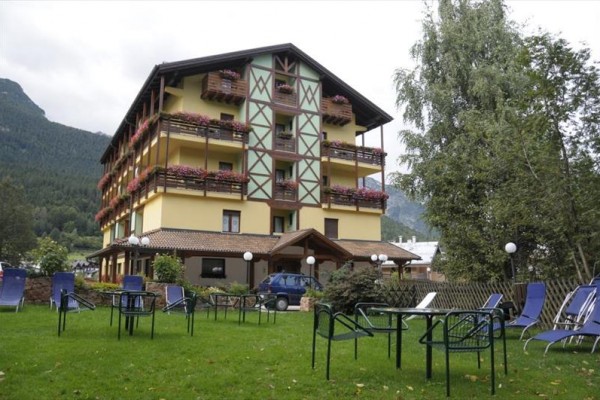 Czteropiętrowy hotel z balkonami i kwiatami otoczony ogrodem z krzesłami.