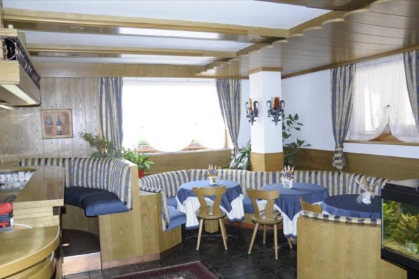 Restauracja z drewnianym wnętrzem, niebieskimi pasiastymi siedziskami i okrągłymi stołami.