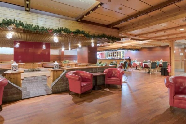 Hotelowa restauracja z drewnianymi sufitami i czerwonymi fotelami.