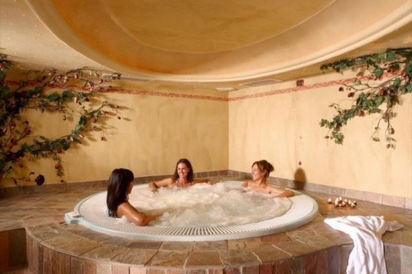 Trzy kobiety relaksują się w jacuzzi otoczonym ozdobnymi roślinami.