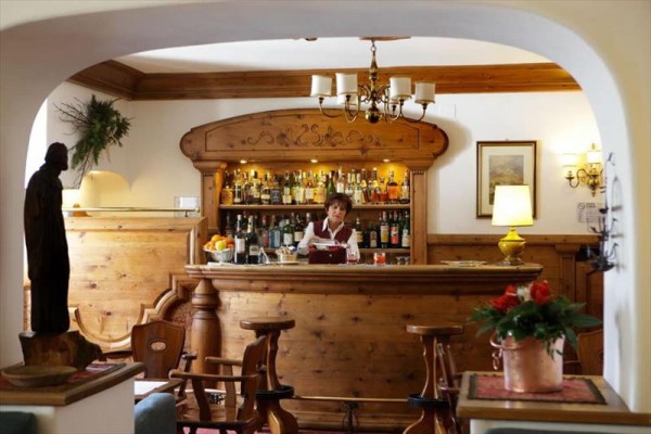 Stylowy drewniany bar z barmanem pośrodku, otoczony butelkami alkoholu i dekoracjami.