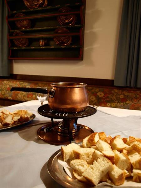 Miedziany garnek do fondue z talerzami kostek chleba na stole.