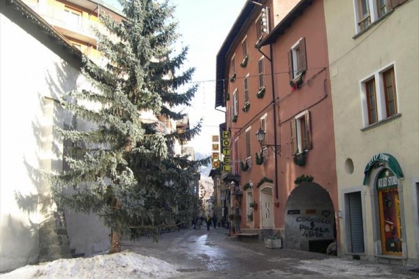 Wąska ulica z hotelem, drzewkiem i śniegiem na ziemi.
