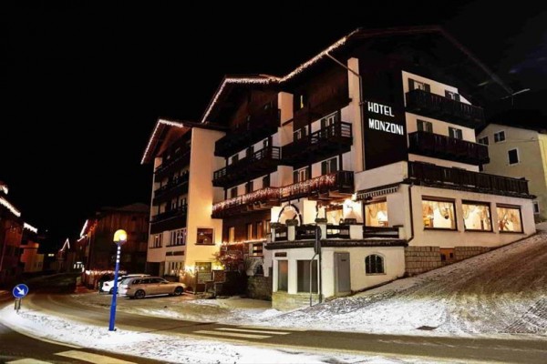 Hotel Monzoni nocą z ozdobami świątecznymi i zaśnieżoną okolicą.