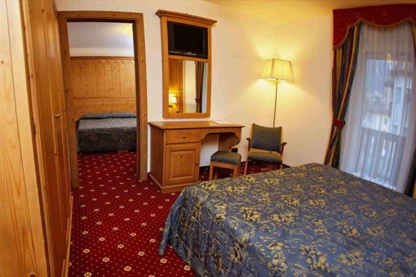 Pokój hotelowy z łóżkiem małżeńskim, biurkiem i telewizorem na ścianie.