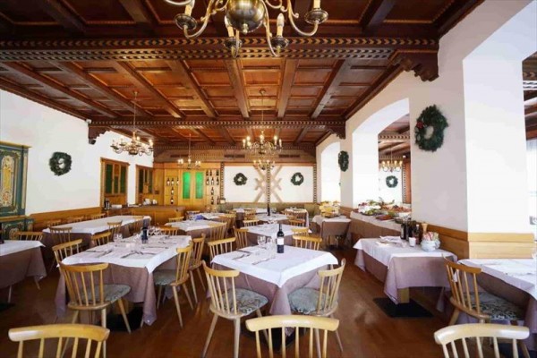 Restauracja z drewnianym sufitem, okrągłymi stolikami i świątecznymi dekoracjami.