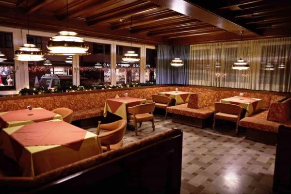 Restauracja z drewnianymi sufitami, zasłonami i nakrytymi stołami z obrusami.