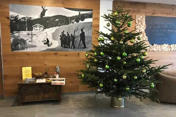 Choinka ozdobiona zielonymi kulami stoi obok zawieszonej czarno-białej fotografii na drewnianej ścianie.