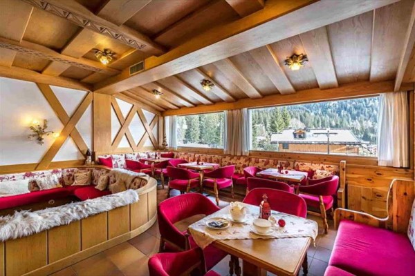 Wnętrze drewnianej restauracji z czerwonymi krzesłami i widokiem na ośnieżone drzewa.