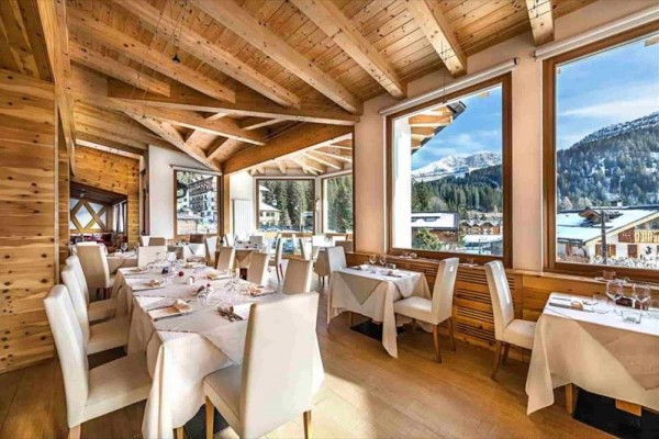 Restauracja z drewnianym wnętrzem i dużymi oknami z widokiem na ośnieżone góry.