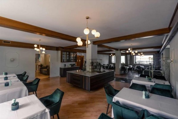 Nowoczesna restauracja z drewnianą podłogą, białymi obrusami i zielonymi krzesłami.