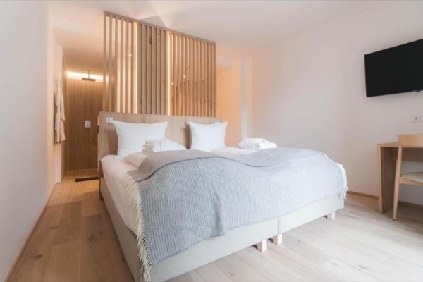 Nowoczesny pokój hotelowy z podwójnym łóżkiem, drewnianą ścianą, telewizorem i biurkiem.