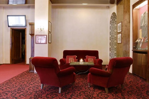 Kącik z czerwonymi fotelami i sofą w eleganckim wnętrzu z dywanami i świecą na stoliku.