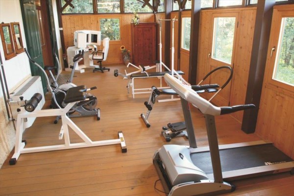 Mała siłownia z różnym sprzętem fitness i drewnianą podłogą.