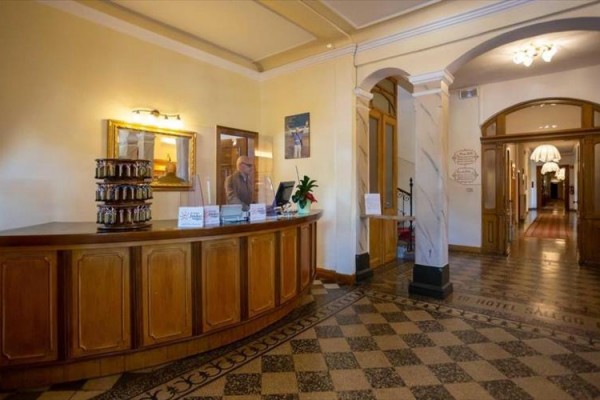 Recepcja hotelowa z drewnianym kontuarem i pracownikiem w garniturze.