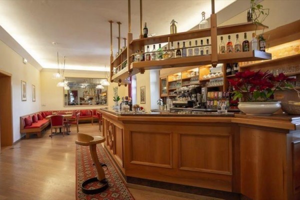 Bar z drewnianym kontuarem i półkami z napojami, w tle czerwone kanapy.