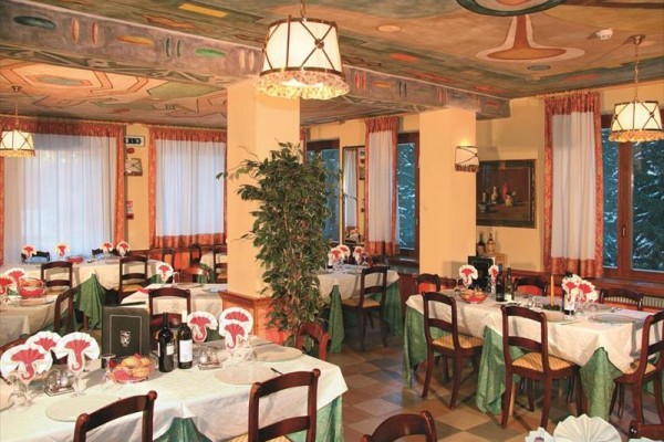Elegancka restauracja z nakrytymi stołami, materiałowymi serwetkami i butelkami wina, we wnętrzu z ozdobnym sufitem i dużymi oknami.