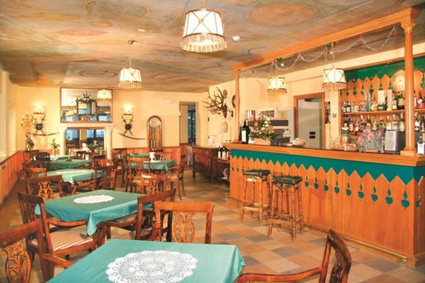 Rustykalne wnętrze restauracji z drewnianymi stołami i filarami, sufit zdobiony malowidłami.