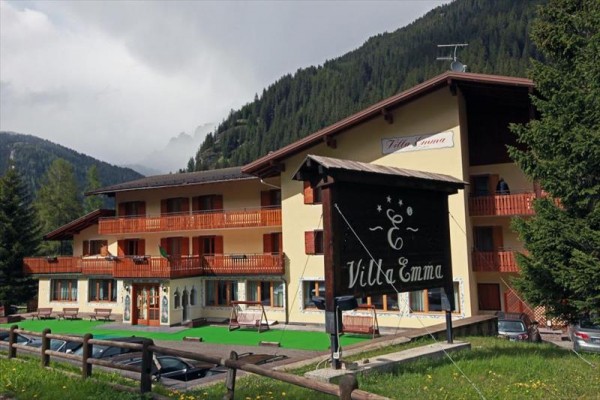 Górski hotel Villa Emma z żółtą fasadą i drewnianymi balkonami otoczony lasami.