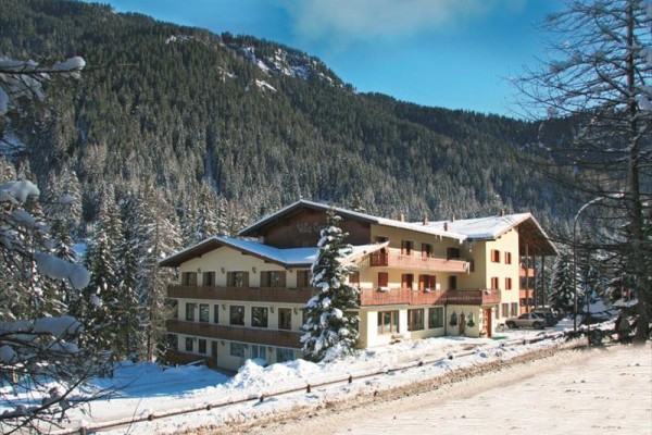 Hotel pośród ośnieżonego lasu z górami w tle.