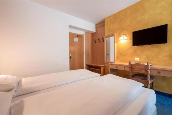 Pokój hotelowy z łóżkiem małżeńskim, telewizorem i lustrem na żółtej ścianie.