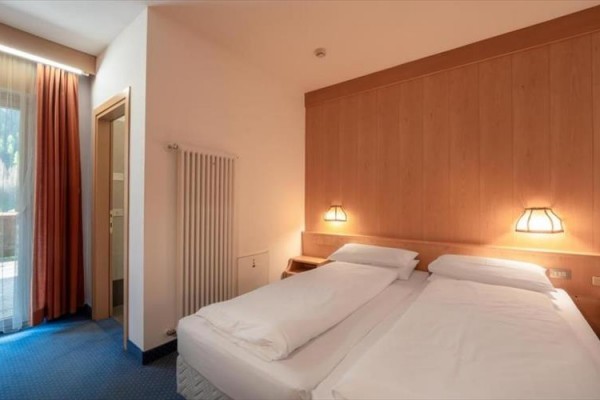Pokój hotelowy z dwoma pojedynczymi łóżkami obok siebie, oświetlony lampkami na ścianie.