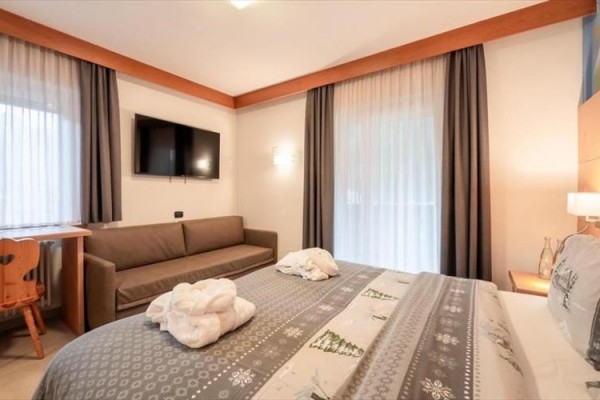 Pokój hotelowy z łóżkiem małżeńskim, kanapą i dużym telewizorem na ścianie.