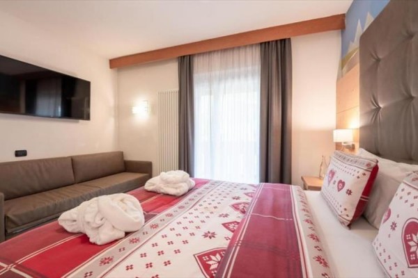 Nowocześnie urządzony pokój hotelowy z dużym łóżkiem, sofą i telewizorem na ścianie.