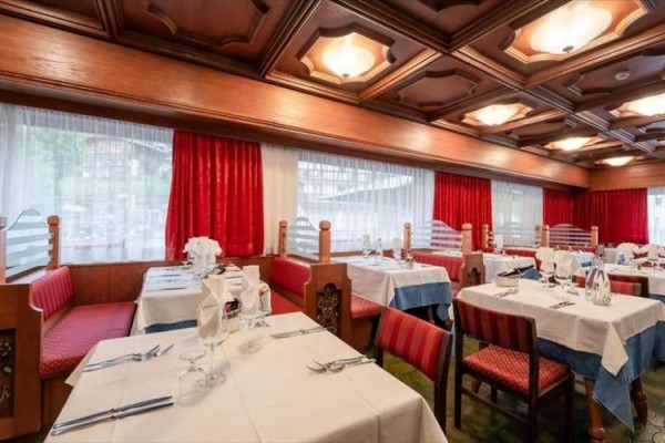 Restauracja z drewnianym sufitem i nakrytymi stołami z białymi obrusami i czerwonymi krzesłami.