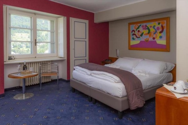 Pokój hotelowy z podwójnym łóżkiem, kolorowym obrazem na ścianie i stołem z krzesłami przy oknie.