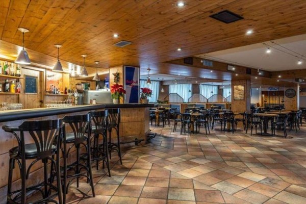 Stylowe wnętrze restauracji z drewnianym wystrojem, barem i pustymi stolikami.
