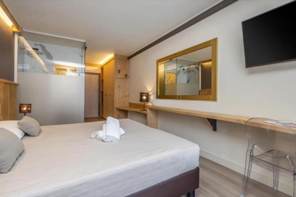 Nowoczesny pokój hotelowy z podwójnym łóżkiem, telewizorem i lustrem na ścianie.